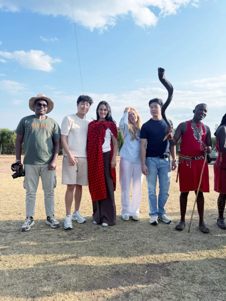 Safari guests with Maasai hosts beside a wildlife sculpture