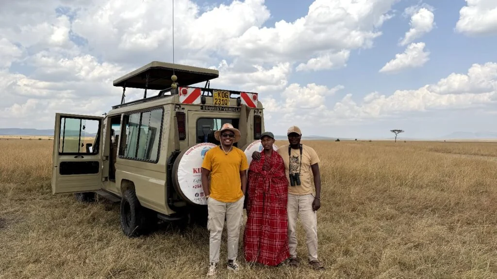 Guests and a Maasai host beside an open-roof safari vehicle